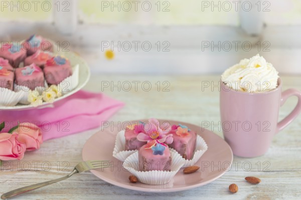 Pink petit fours and a cup of coffee and cream on a table