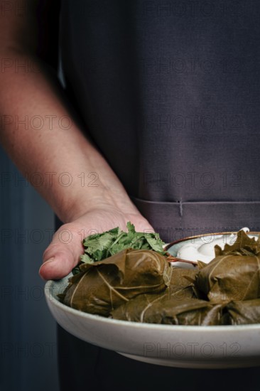 A man holds a plate in his hands, a dolma with sauce and lemon