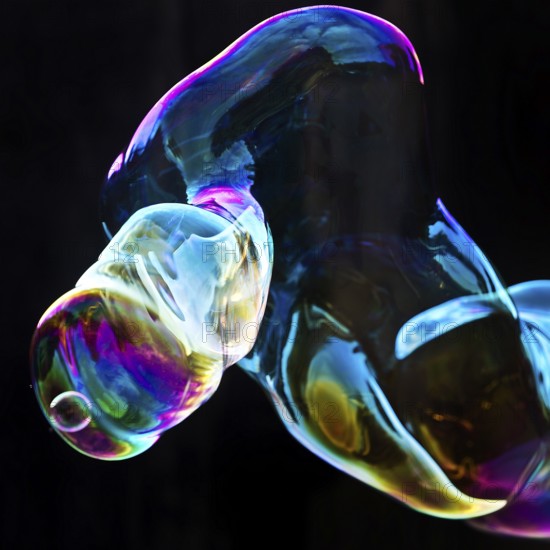 Large, iridescent soap bubble tube in the colours of the rainbow against a black background, Recklinghausen, North Rhine-Westphalia, Germany