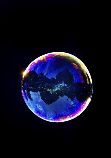 A shimmering and floating soap bubble in the colours of the rainbow against a black background, Recklinghausen, Germany
