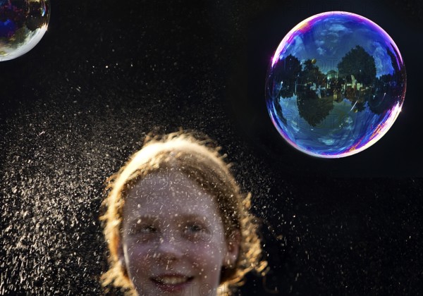 A girl is happy about a shimmering and floating soap bubble in front of a black background, Recklinghausen, Germany