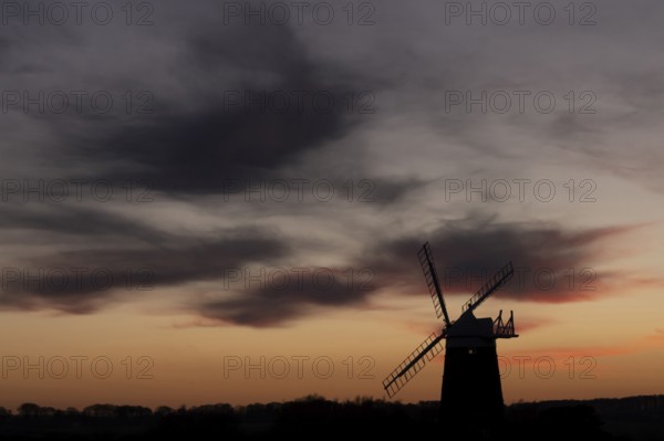 Windmill silhouette at sunset with a red sky and dark clouds, Burnham Ovary Staithe, Norfolk, England, United Kingdom