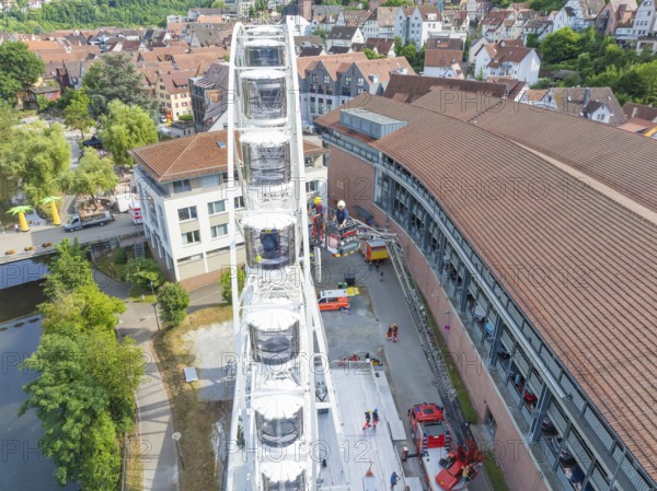 View of a Ferris wheel in a city with surrounding buildings and people in summer, fire brigade exercise for gondola rescue, Germany