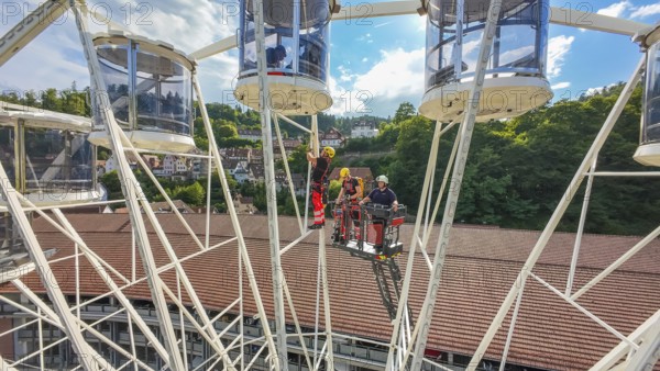 Workers in a Ferris wheel with lifting platform, surrounded by green hills and blue sky, fire brigade exercise for gondola rescue, Germany
