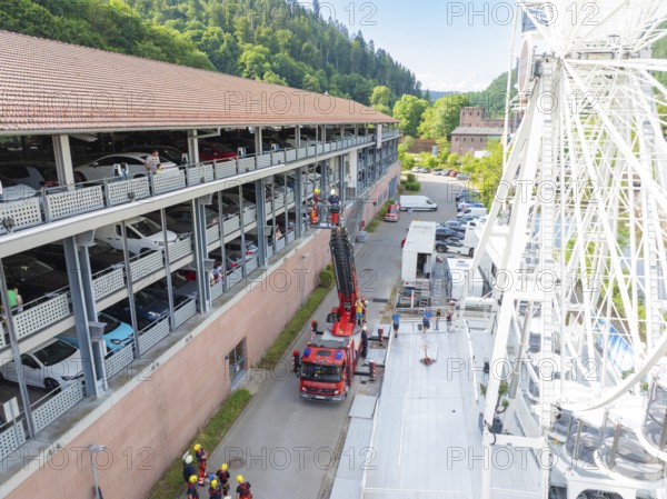 Ferris wheel near a multi-storey car park, fire engines and people in sunny weather, fire brigade exercise for gondola rescue, Germany