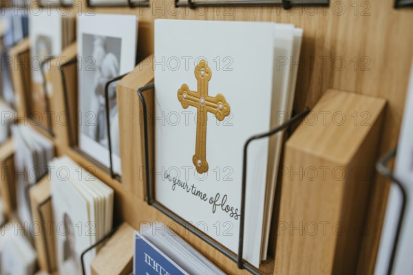 Condolence card with In your time of loss text and golden religious cross displayed in a card rack at a shop. Generative ai, AI generated