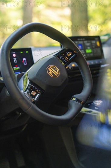 Modern tech displays and steering wheel in the car interior, forest and sunlight in the background, MG 4, Deer E- Car Sharing, Calw district, Germany