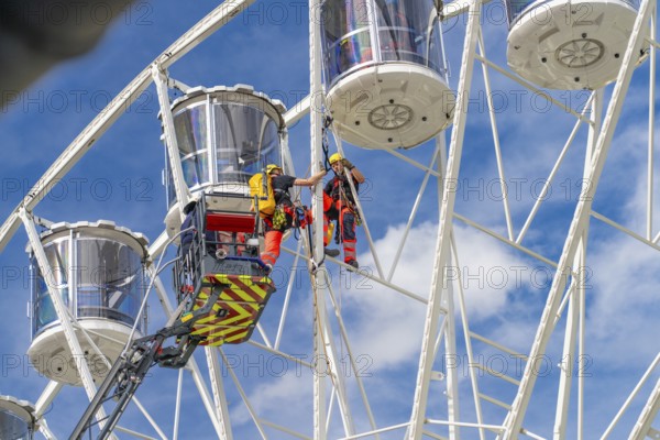 Workers in climbing gear carry out a rescue operation on the Ferris wheel, fire brigade exercise for gondola rescue, Germany