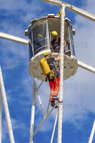 Two workers in safety equipment during maintenance work on a Ferris wheel in a cabin, fire brigade exercise for gondola rescue, Germany