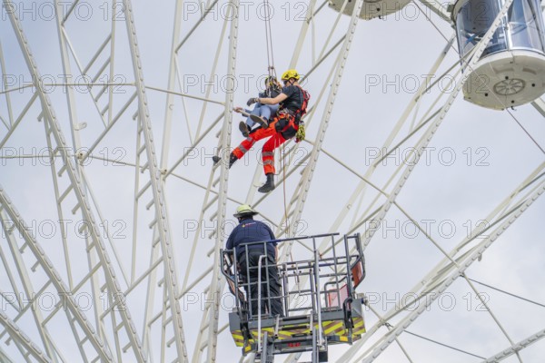 Firefighters rescue person by abseiling from Ferris wheel, fire brigade exercise for gondola rescue, Germany