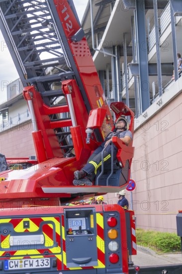 Firefighter resting on an extended lifting platform next to a building, fire brigade exercise for gondola rescue, Germany