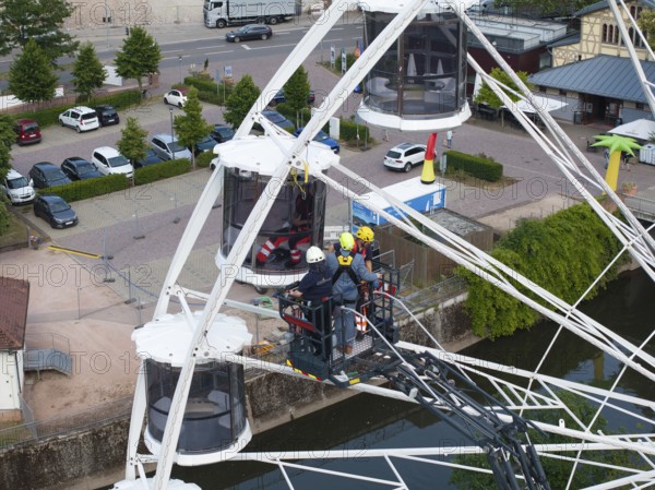 Firefighters during a rescue exercise on a Ferris wheel in an urban environment with parked cars, fire brigade exercise for gondola rescue, Germany