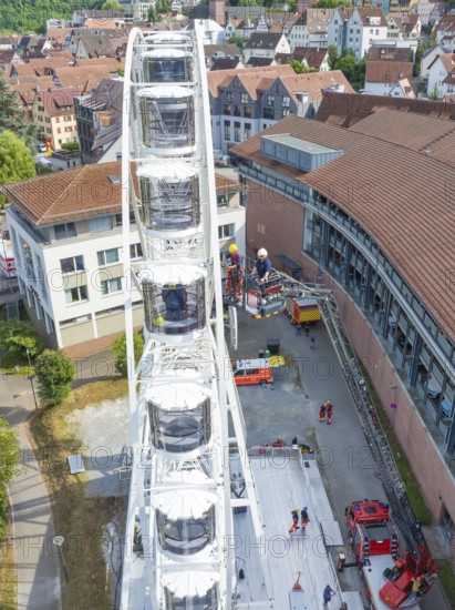 Rescue operation on a Ferris wheel with emergency vehicles in an urban setting with red roofs, fire brigade exercise for gondola rescue, Germany