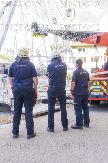 Three firefighters in uniforms standing in front of emergency vehicle with lifting platform, fire brigade exercise for gondola rescue Ferris wheel, Calw, Germany