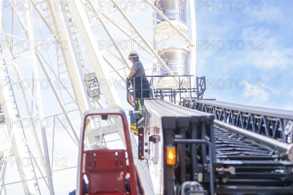 Firefighter on a lifting platform next to a Ferris wheel in front of a clear sky, fire brigade exercise for gondola rescue Ferris wheel, Calw, Germany