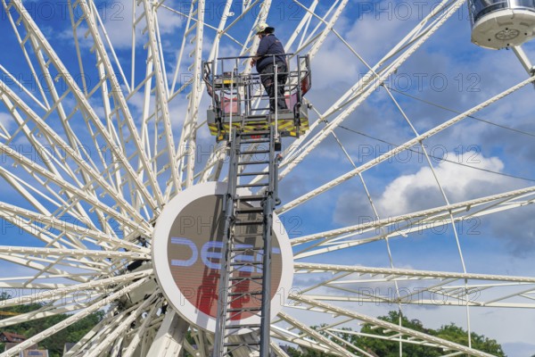 A worker on a ladder, the Ferris wheel and the blue sky characterise the scene, Fire brigade exercise for gondola rescue Ferris wheel, Calw, Germany