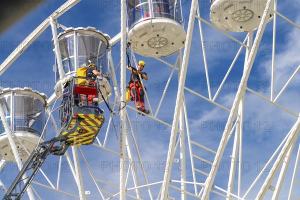 Workers secured on a Ferris wheel during rescue work under blue sky, fire brigade exercise for gondola rescue Ferris wheel, Calw, Germany