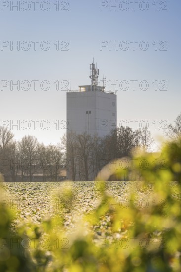 A white communication tower stands in a wintry field, surrounded by trees under a clear, sunny sky, Germany