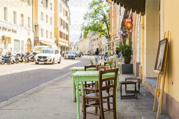 A street café with green wooden chairs in sunny weather in a lively town, Merano, South Tyrol, Italy