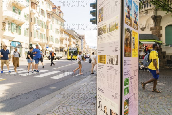 Lively street scene with pedestrians and poster pillar on a sunny day, Merano, South Tyrol, Italy