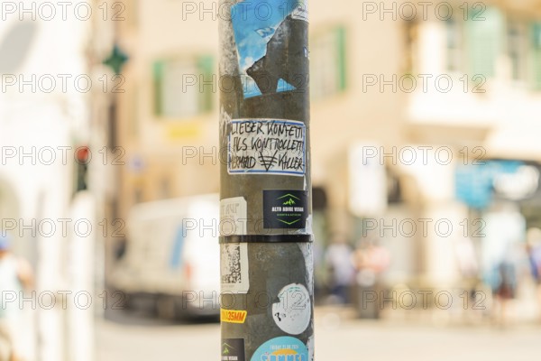 A lamppost with graffiti and stickers in an urban environment with a blurred background, Merano, South Tyrol, Italy