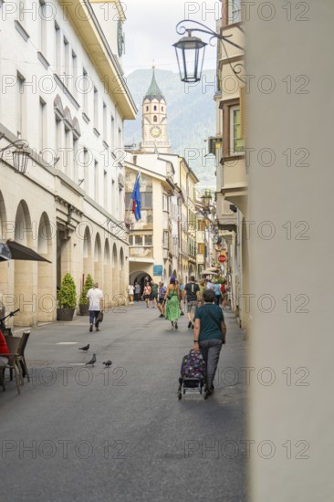 People walking through a historic old town alley with a view of a bell tower, Merano, South Tyrol, Italy