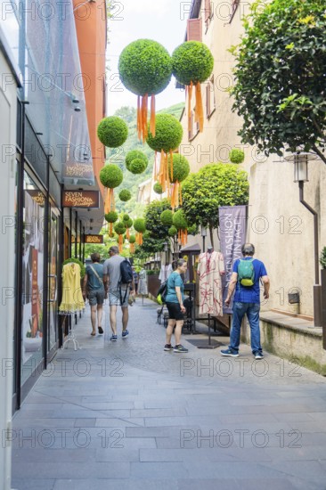 Narrow shopping street with people and decorative baubles on the faÃ§ade, Merano, South Tyrol, Italy