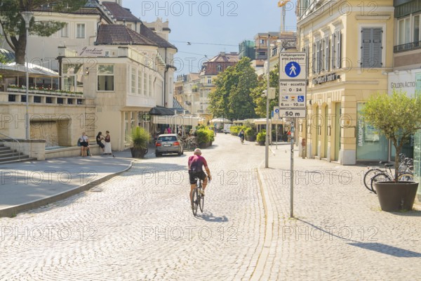Biker riding through sunny cobblestones in a lively town, Merano, South Tyrol, Italy