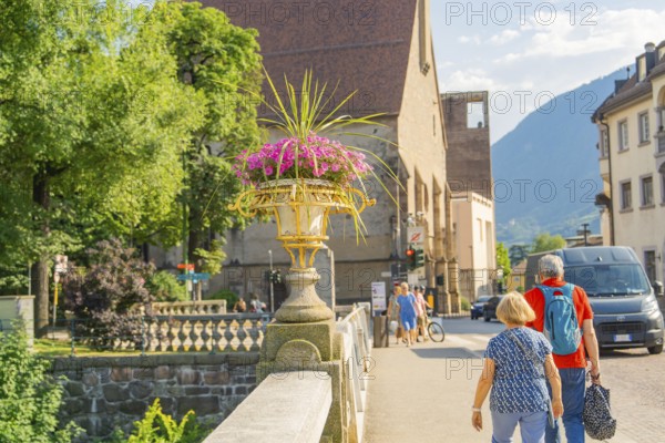 A couple walks across the stone bridge, view of mountains and flowers, Merano, South Tyrol, Italy