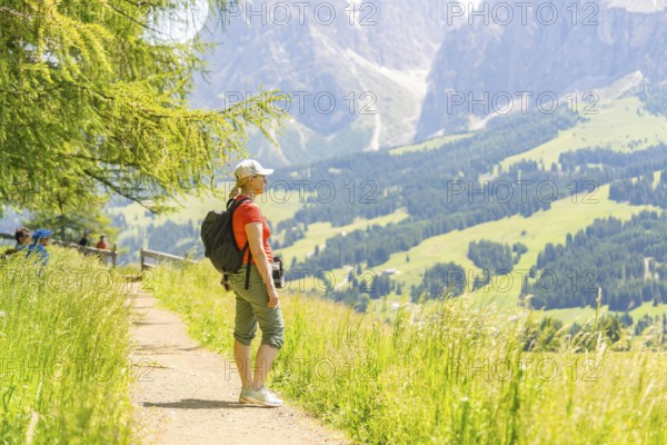 Woman standing on a path and enjoying the wide view of the green mountains, Alpe di Siusi, Dolomites, South Tyrol, Italy