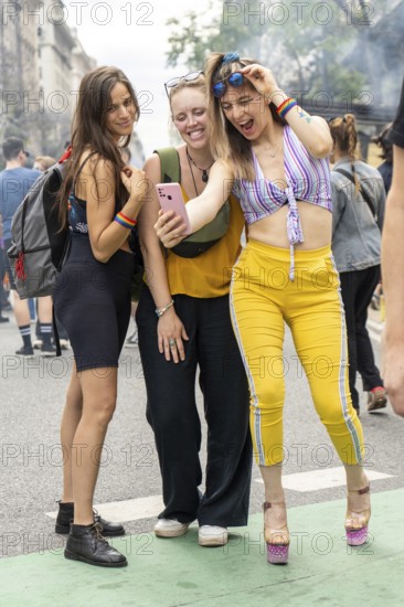 Three cheerful young women wearing rainbow bracelets are taking a selfie with a smartphone during a gay pride parade, celebrating lgbtq rights and community