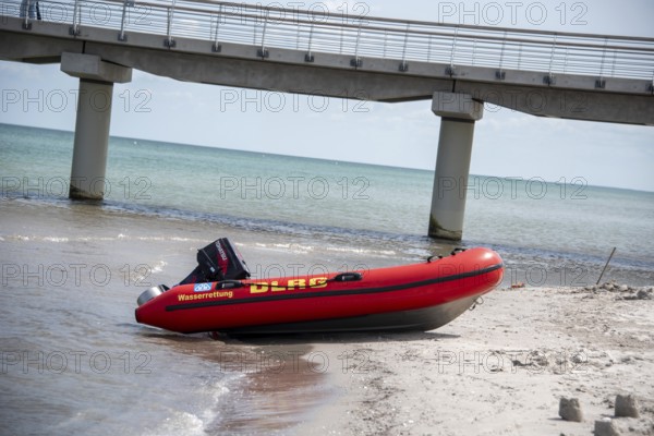 A DLRG lifeboat lies on the beach in front of a bridge with walkers and the sea in the background, Prerow, Mecklenburg-Vorpommern, Germany