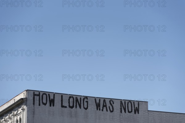 The lettering HOW LONG WAS NOW is emblazoned on the faÃ§ade of a building in Berlin-Mitte, Berlin, Germany