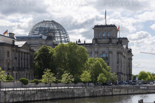 The Reichstag building in Berlin-Mitte, seat of the German Bundestag, rises imposingly behind dense treetops directly on the banks of the River Spree, Berlin, Germany