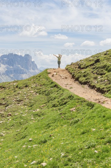 Person hiking on a path with views of rocky mountains and wide skies, Schlehrn hike, Alpe di Siusi, Dolomites, South Tyrol, Italy