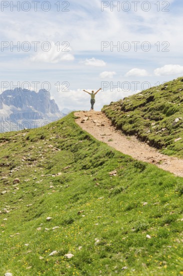 Person opens his arms on a hill path with a view of rocky mountains, Schlehrn hike, Alpe di Siusi, Dolomites, South Tyrol, Italy