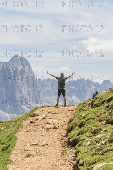Person on a path with outstretched arms in front of a majestic mountain landscape, Schlehrn hike, Alpe di Siusi, Dolomites, South Tyrol, Italy