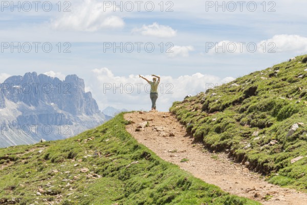Person spreading his arms on a path in front of a majestic mountain scenery, Schlehrn hike, Alpe di Siusi, Dolomites, South Tyrol, Italy