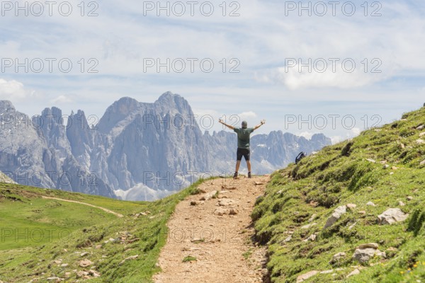 Person with raised arms on a hiking trail in front of an impressive mountain panorama, Schlehrn hike, Alpe di Siusi, Dolomites, South Tyrol, Italy