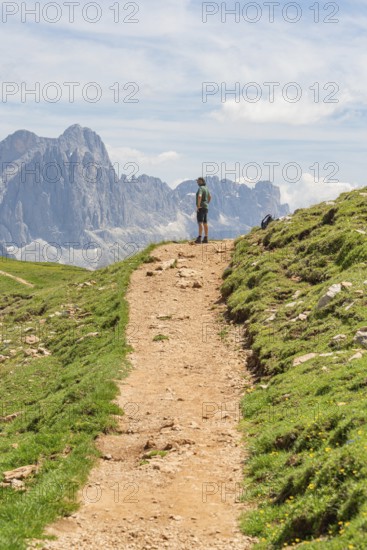 Hiker standing on a path with visible rocks and imposing mountains, Schlehrn hike, Alpe di Siusi, Dolomites, South Tyrol, Italy