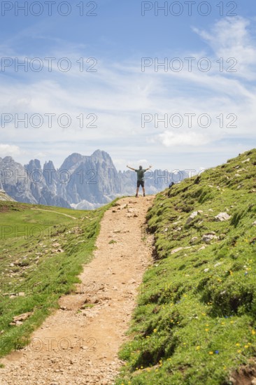 A hiker on a mountain path with outstretched arms in front of an impressive mountain scenery, Schlehrn hike, Alpe di Siusi, Dolomites, South Tyrol, Italy