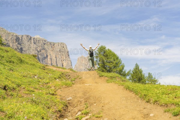 A hiker enjoys a sunny path in a mountainous landscape, Schlehrn hike, Alpe di Siusi, Dolomites, South Tyrol, Italy