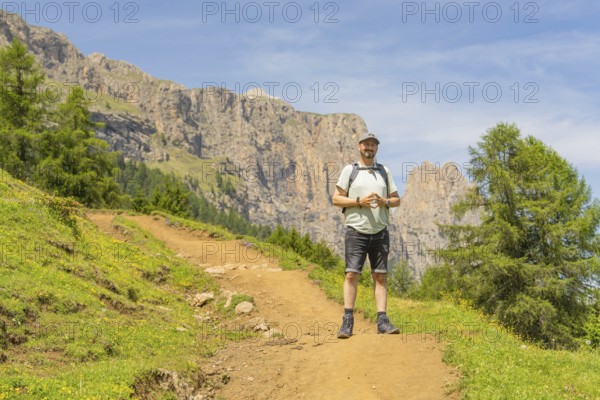 A hiker with a rucksack on a path against a rocky mountain backdrop in fine weather, Schlehrn hike, Alpe di Siusi, Dolomites, South Tyrol, Italy