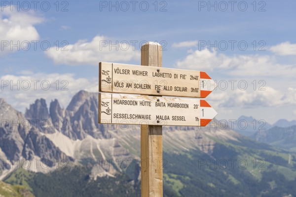 Wooden signpost with directions, mountain panorama in the background under a clear sky, hike to the Schlehrn, Seiser Alm, Dolomites, South Tyrol, Italy