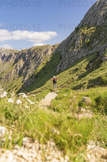 Person hiking on a path between steep slopes, green nature and blue sky, hike to the Schlehrn, Seiser Alm, Dolomites, South Tyrol, Italy