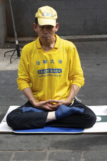 Falun Dafa or Falun Gong man meditating sitting cross legged, Gerrard Street, Chinatown, West End, London, England, UK