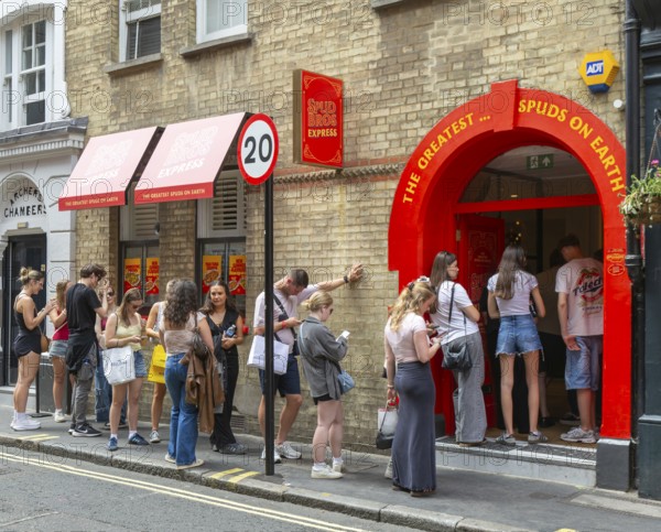 Queue line of people waiting at entrance Spud Bros Express fast-food takeaway, Soho, London, England, UK