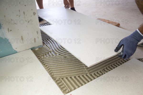 Tile laying: Tiler lays large light-coloured floor tiles