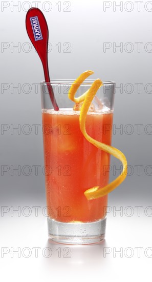 Campari cocktail in a long drink glass on ice with orange zest as garnish against a white background, studio shot