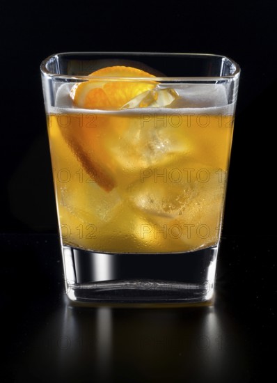 Cocktail in a tumbler on ice with half a slice of orange as garnish against a black background, studio shot